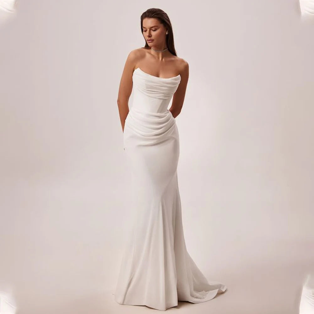 Woman wearing a strapless white wedding dress on a plain backgrounBoho Wedding Dress Dainty Structured Strapless Mermaid Bridal Gown, This refined mermaid wedding gown, crafted from smooth crepe satind