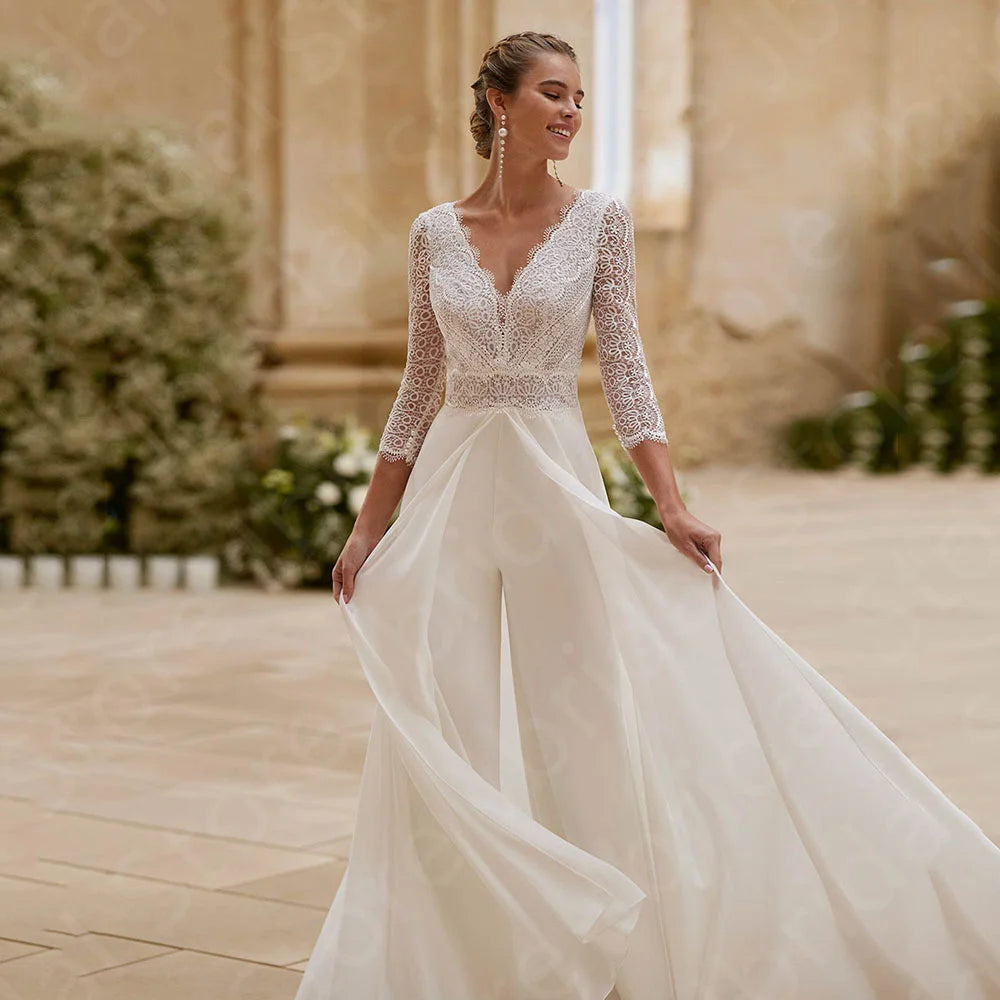 Woman in a white wedding  jumpsuit dress with lace detailing standing outWedding Jumpsuit Lace Bridal Pants Suit, This elegant wedding dress jumpsuit combines sophistication and comfort with a delicate lace bodice doors.