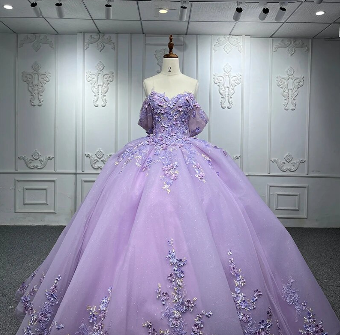 Purple Quinceanera flower bow ball gown dress featuring floral embellishments and off-the-shoulder cuffs.