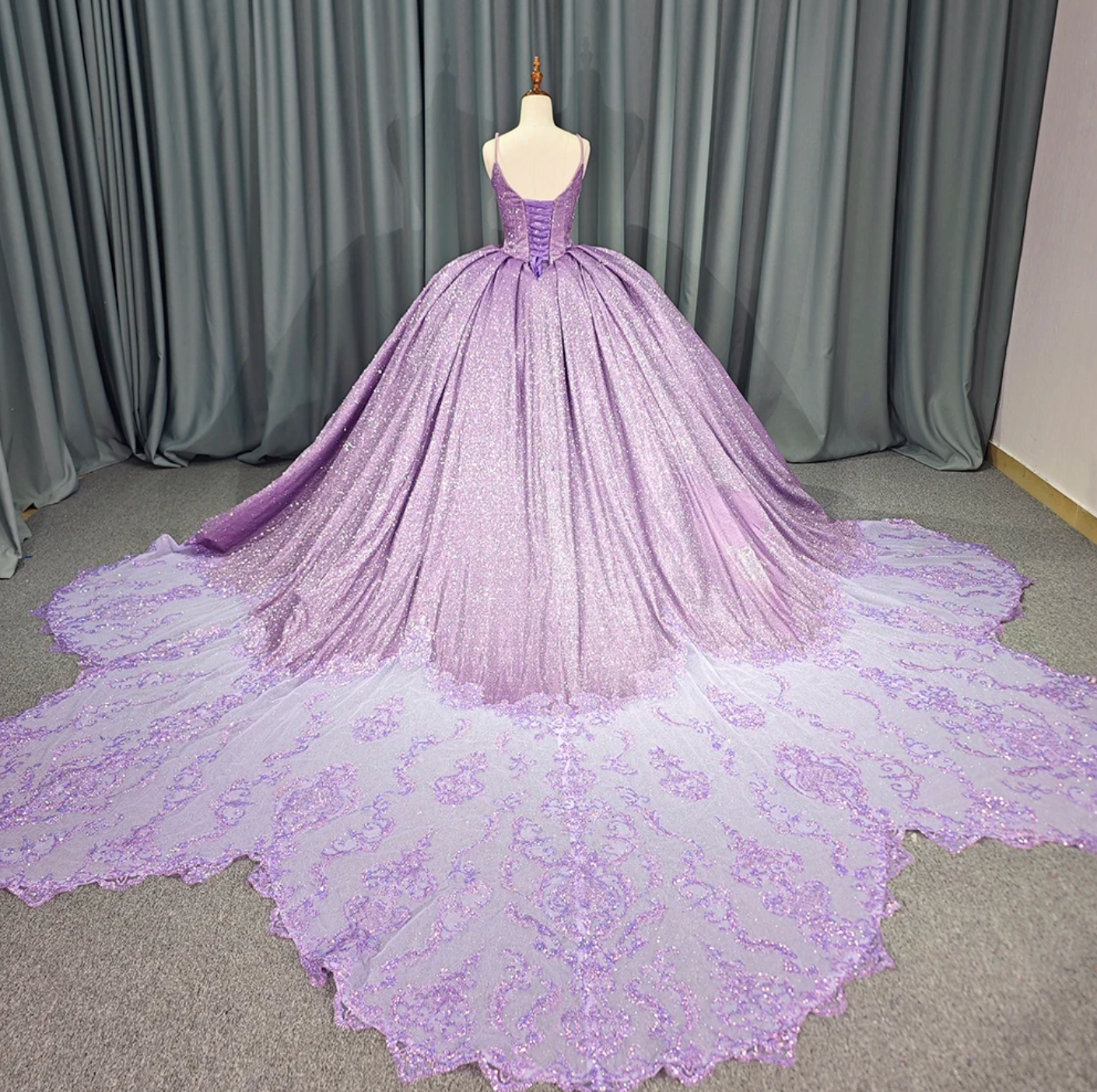 Purple shiny quinceanera dress with voluminous skirt and lace-trimmed train, showcased from the back.