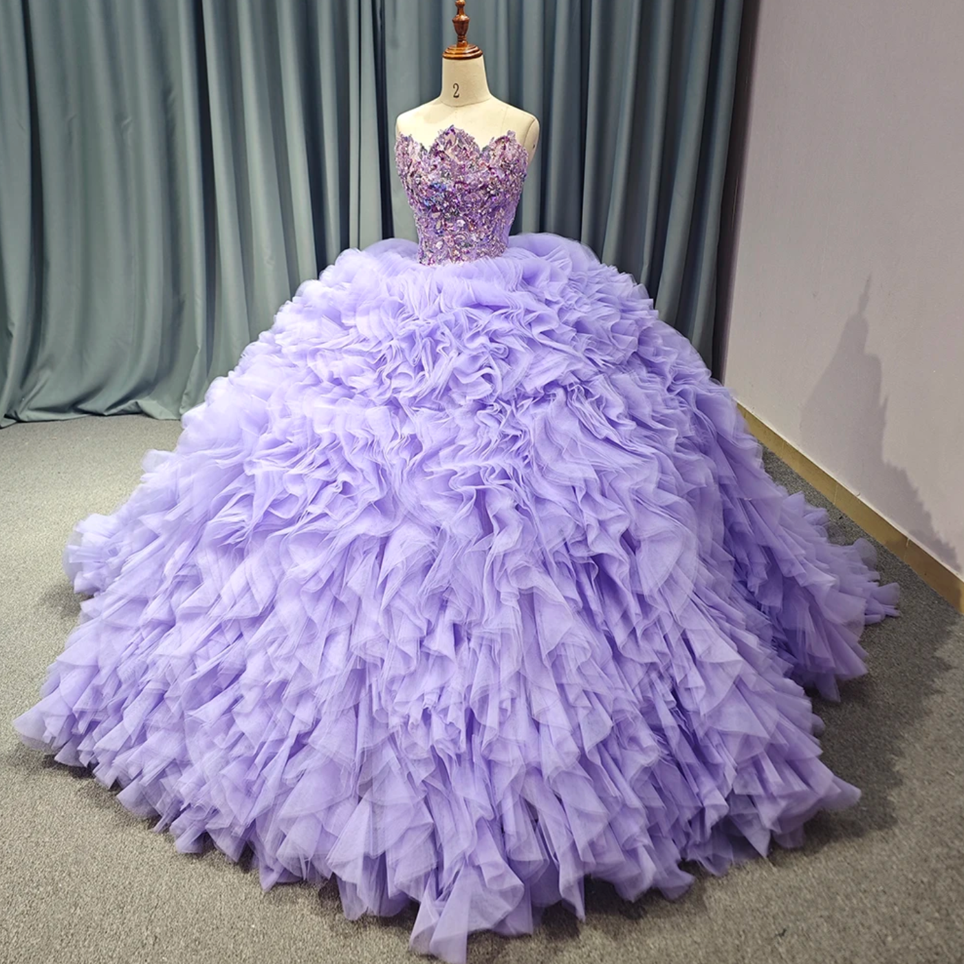 Stunning purple Quinceanera ball gown with tulle ruffles and hand-beaded bodice on a mannequin.