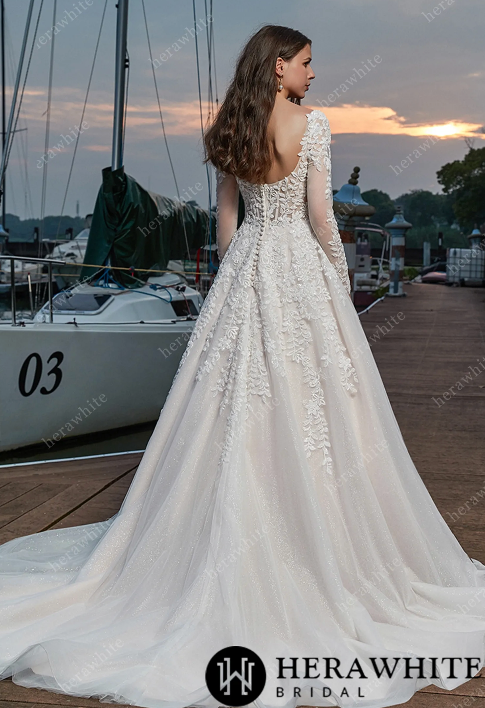 Elegant long sleeve sweetheart wedding dress with vine lace details, showcased on model by the water.