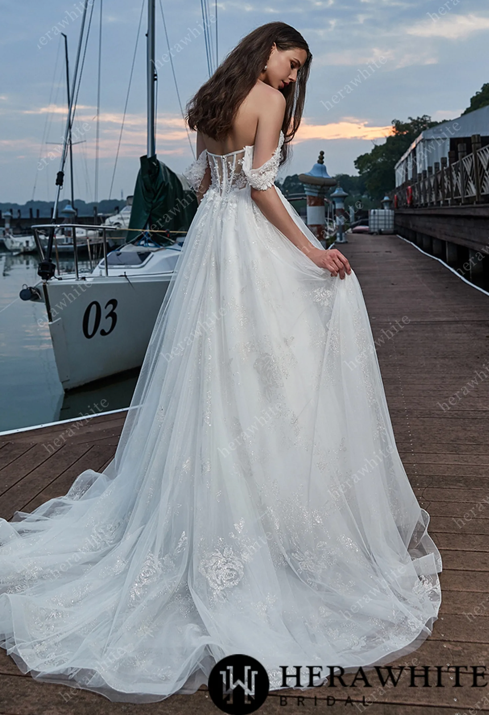 Elegant off shoulder sweetheart wedding dress with voluminous skirt, showcasing lace details against a scenic waterfront backdrop.
