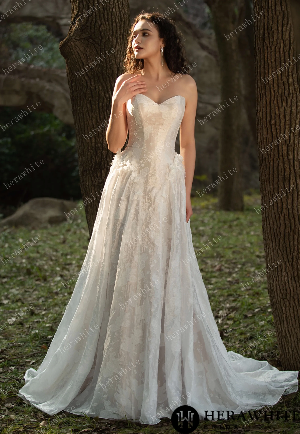 Elegant floral jacquard wedding dress with 3D flower appliqués, flowing silhouette, and basque waistline, outdoor setting.