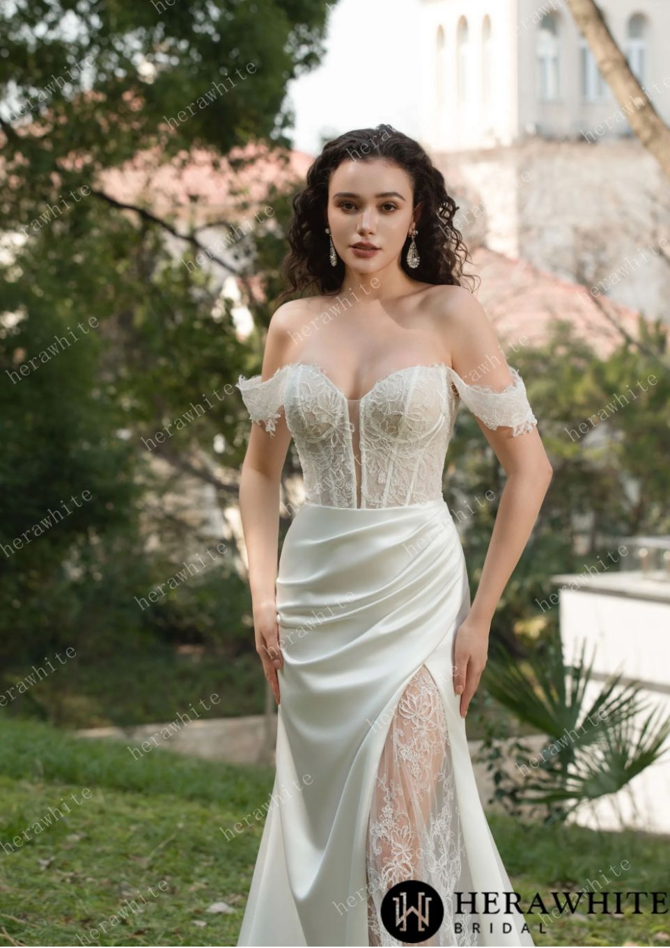 Elegant lace wedding dress with off-the-shoulder straps and sweetheart neckline in a beautiful outdoor setting.