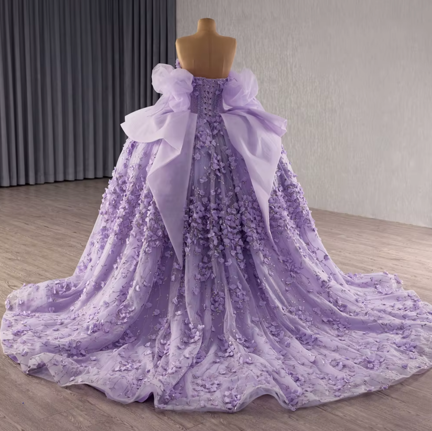 Back view of a lilac purple off shoulder quinceanera dress with intricate beading and elegant side ruffles.