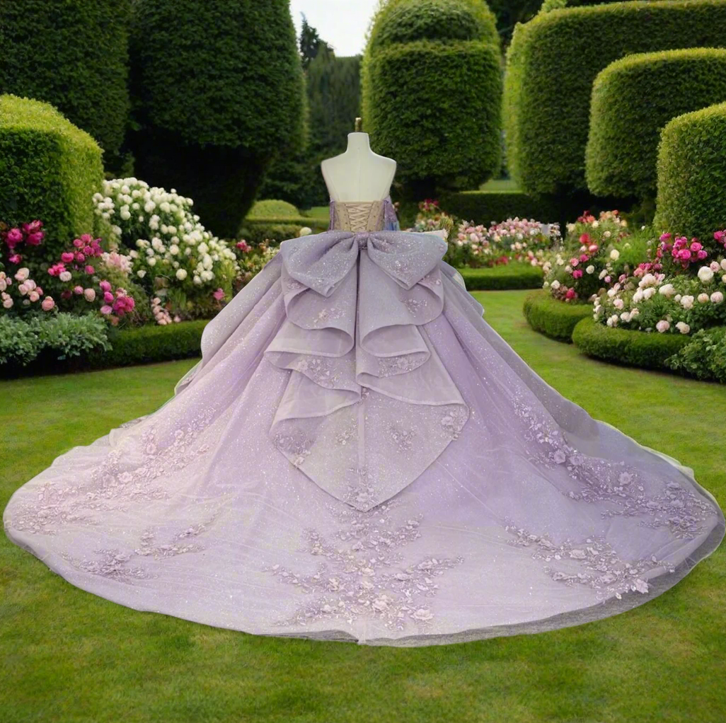 Lilac purple off-shoulder Quinceañera dress with floral embroidery and peplum waist, showcased in a garden setting.