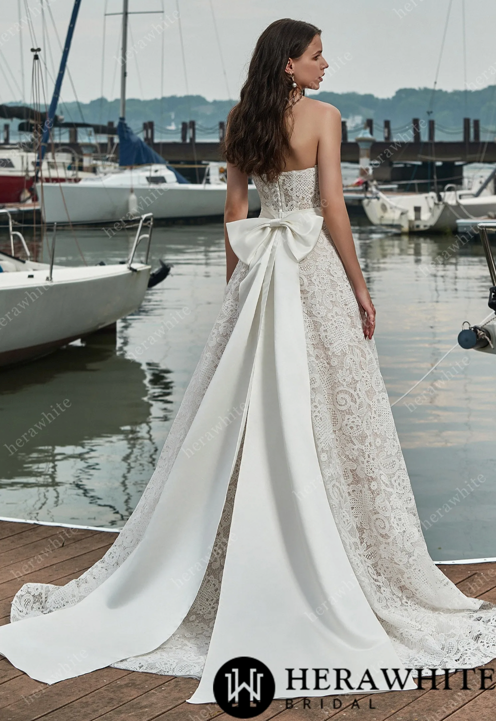 Back view of a strapless lace wedding dress with a large detachable bow, showcasing the A-line silhouette near a marina.