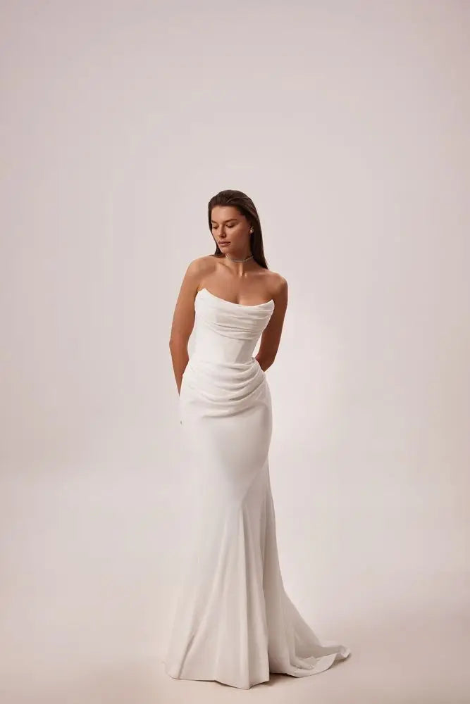 Woman wearing a strapless white wedding dress on a plain backgrBoho Wedding Dress Dainty Structured Strapless Mermaid Bridal Gown, This refined mermaid wedding gown, crafted from smooth crepe satinound