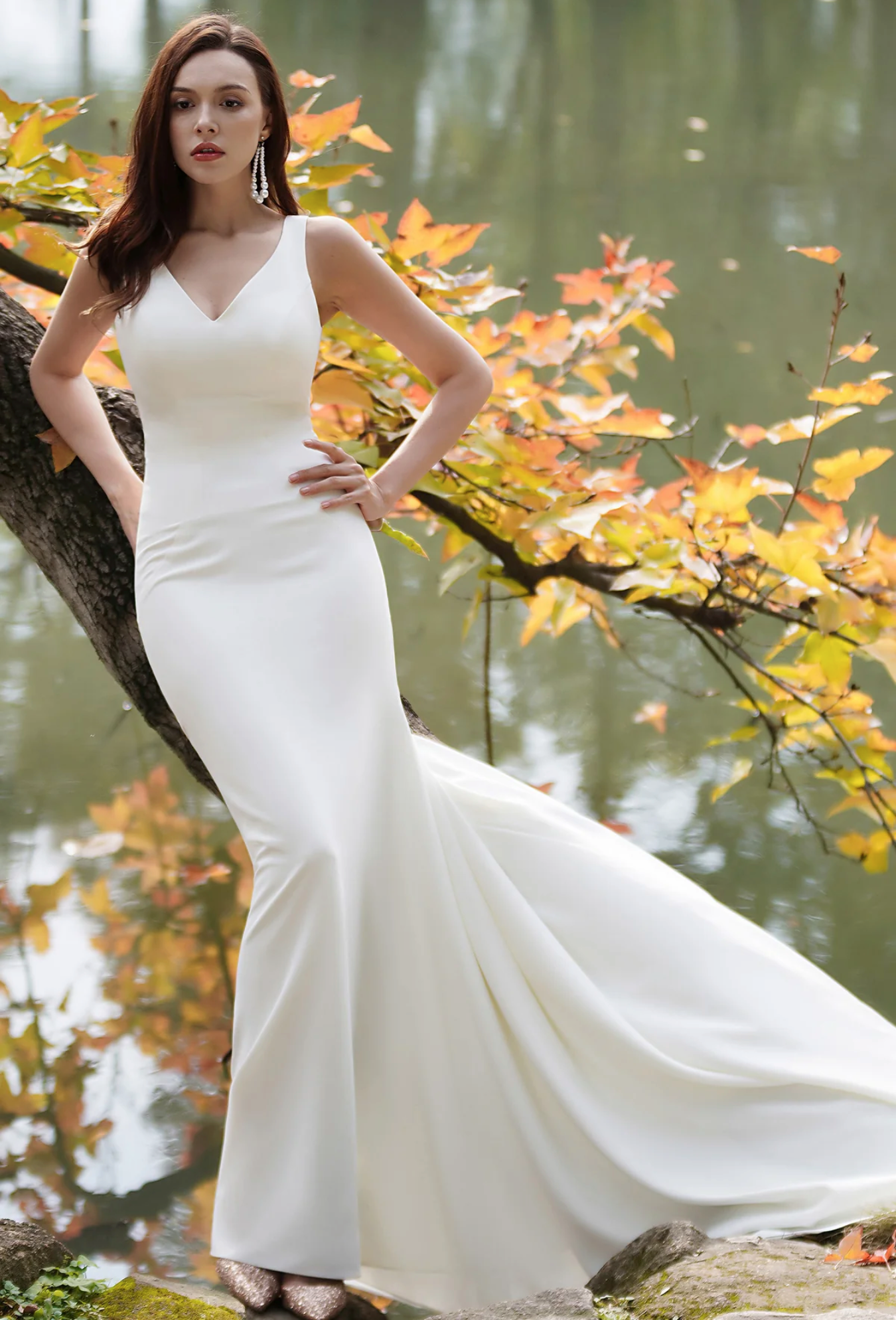 Elegant fit-and-flare wedding dress with a deep-V back, showcased against autumn foliage in a serene outdoor setting.