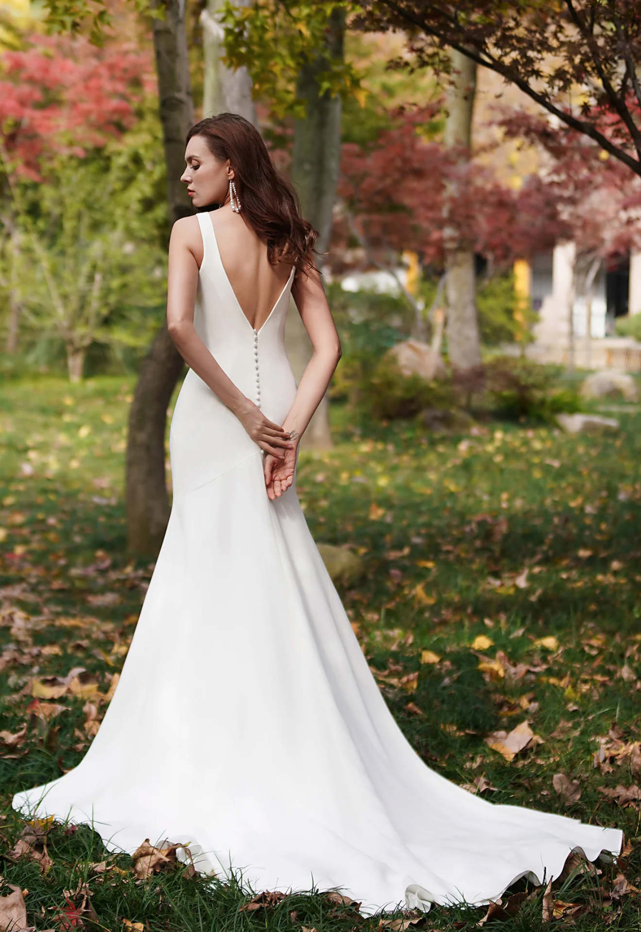 Elegant ivory fit-and-flare wedding dress with a deep-V back and button accents, showcased in a picturesque outdoor setting.